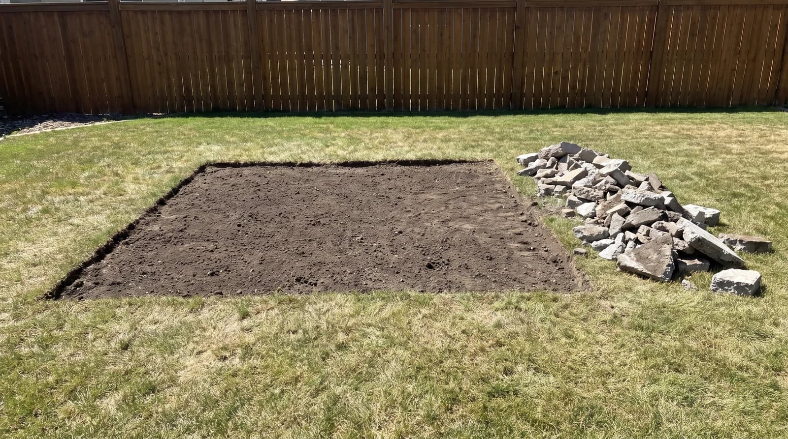 Bare graded dirt where a concrete patio was removed in a Meridian, Idaho backyard, with broken concrete chunks stacked neatly along one edge