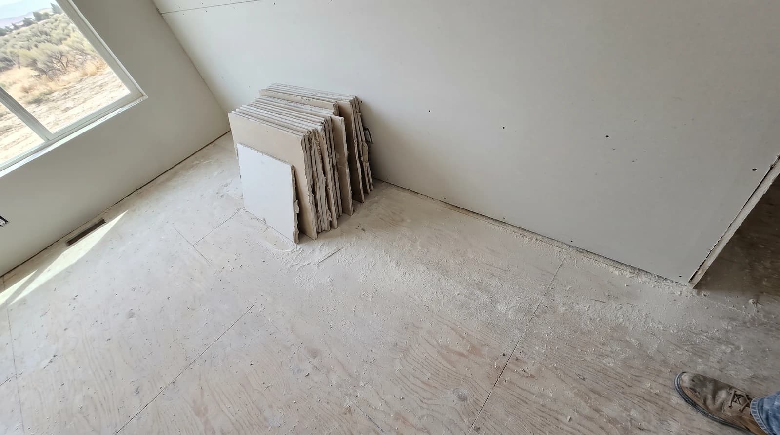 Drywall offcuts stacked in a neat pile inside an empty remodeled room in Eagle, Idaho, with fine construction dust settled on the bare subfloor