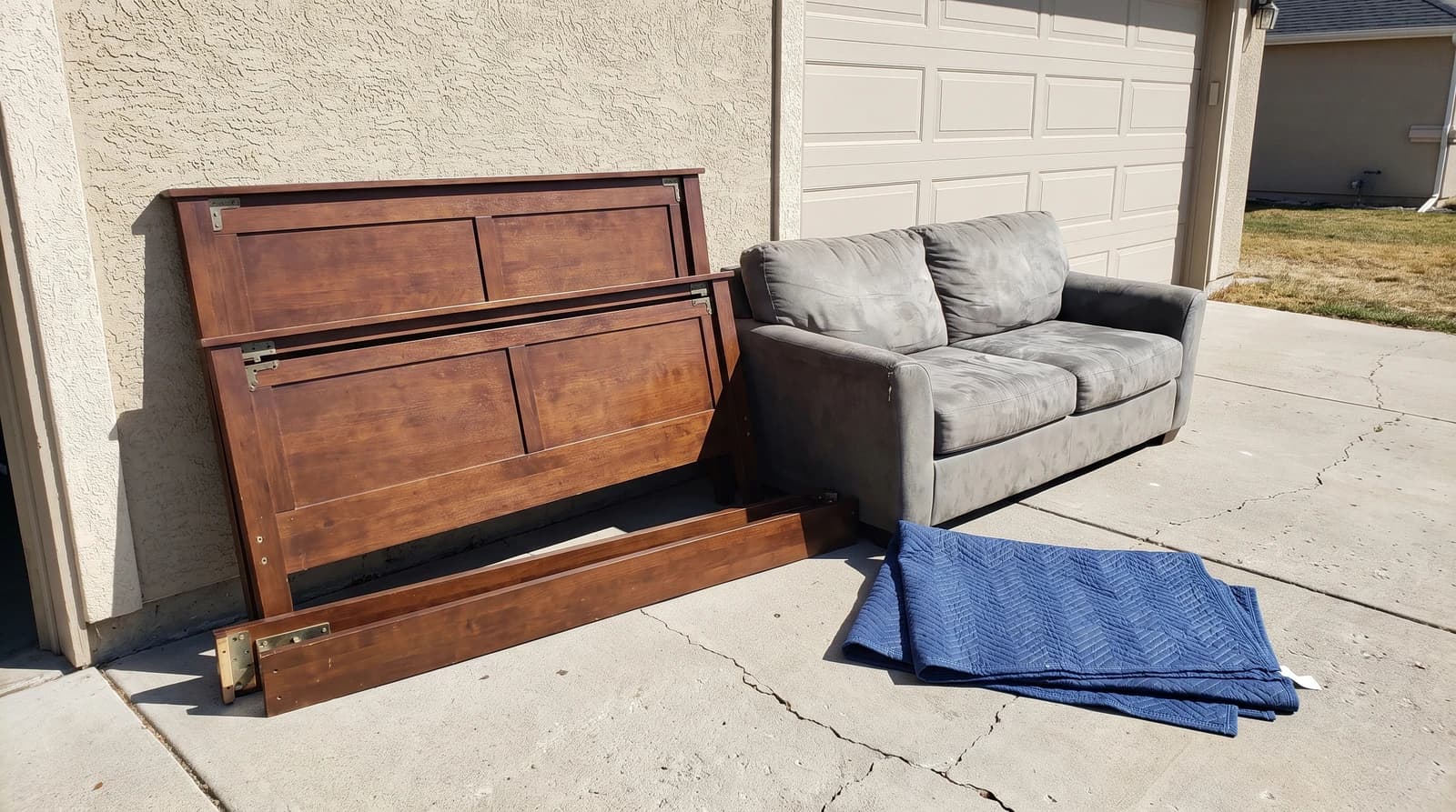 Old sofa and disassembled bed frame set out on a driveway for furniture removal at a home in Kuna, Idaho