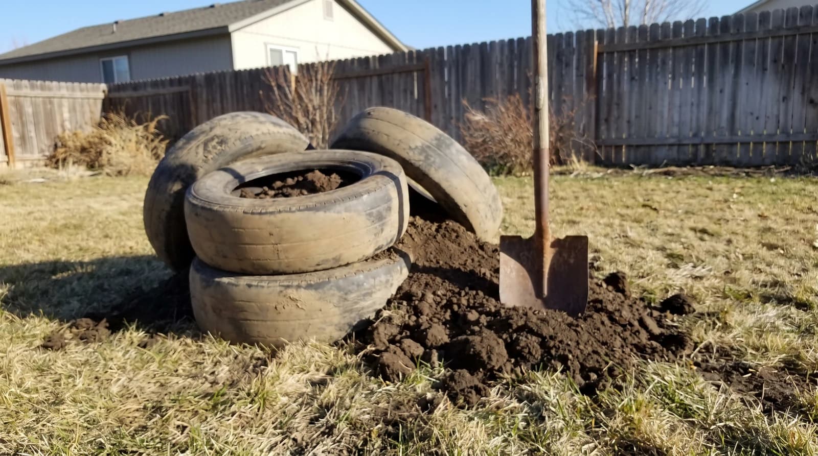 Stack of old dirt-filled tires pulled from a backyard garden during tire removal in Caldwell, Idaho, with a shovel standing in the soil nearby