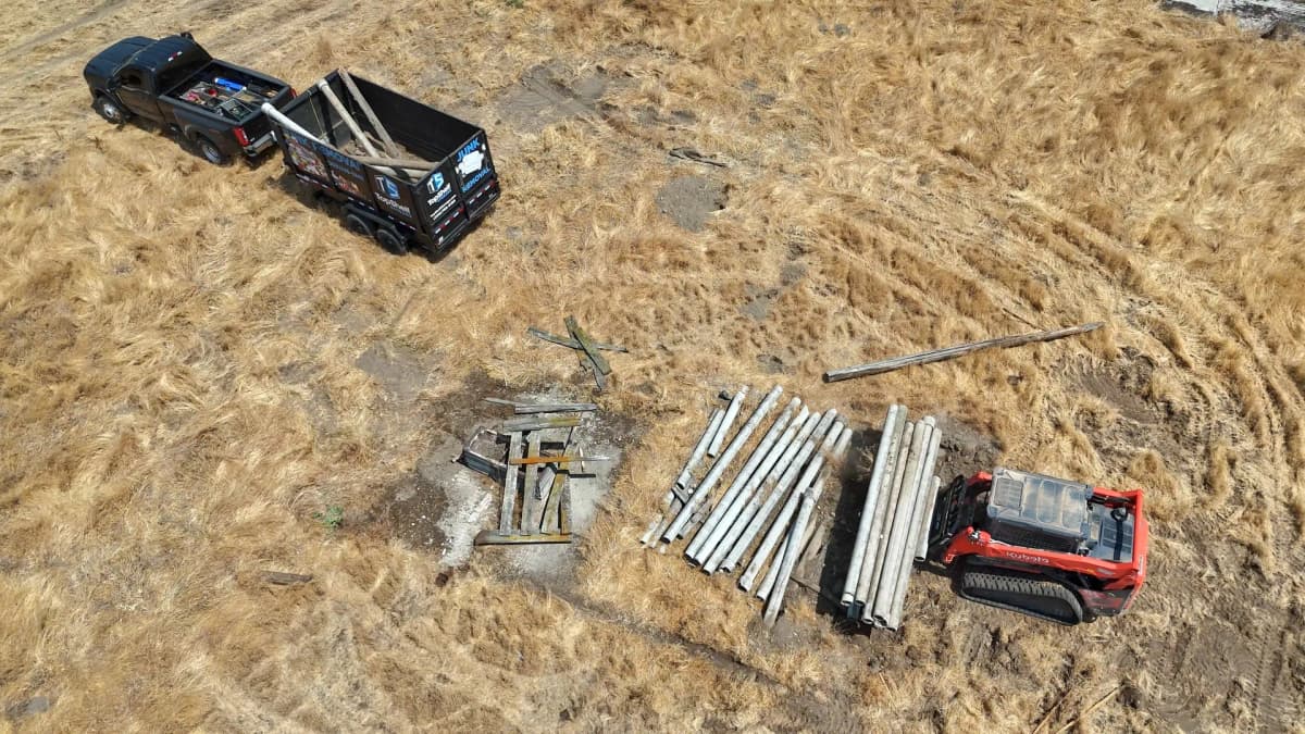 Aerial view of Top Shelf crew removing concrete posts with a Kubota skid steer and branded dump trailer during a property cleanout near Crimson Point in Kuna Idaho