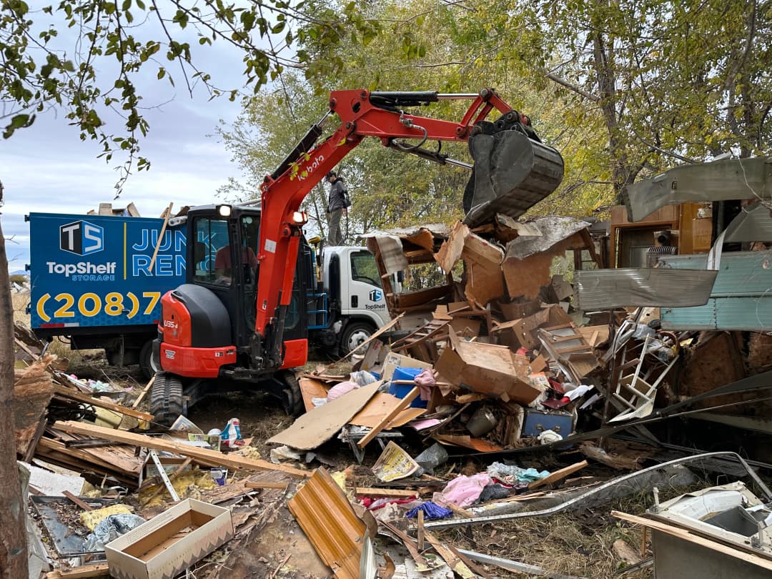 Top Shelf Kubota excavator demolishing an old RV with branded junk removal truck on a rural property in Nampa Idaho