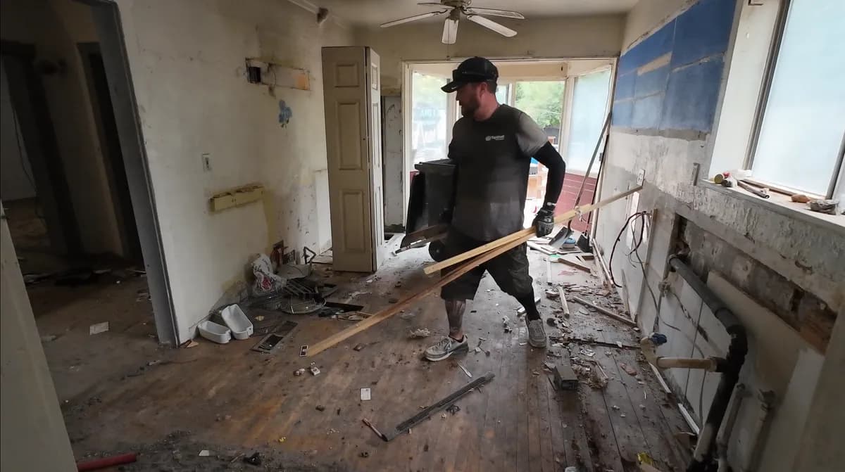 Top Shelf crew member carrying lumber and construction debris out of a gutted house during a renovation cleanout in Nampa Idaho