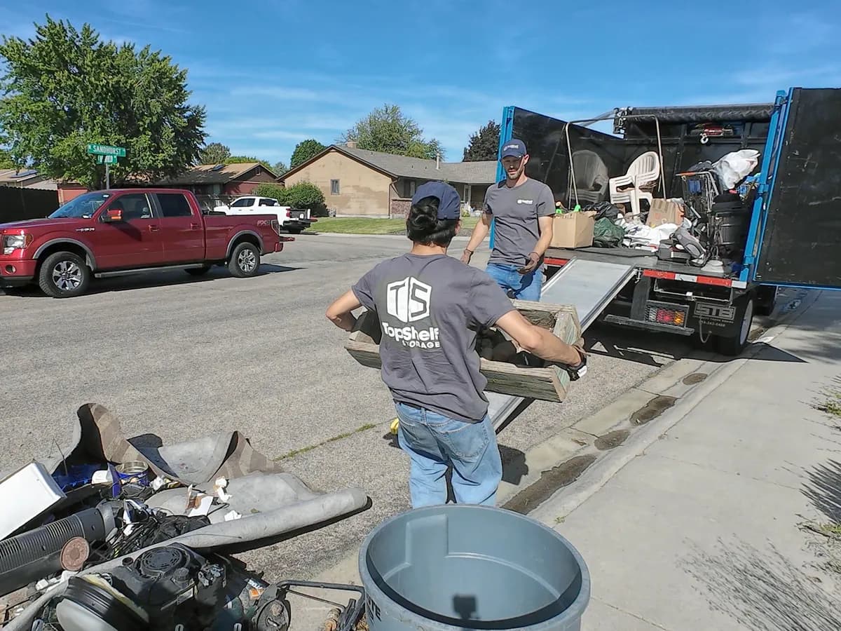 Two Top Shelf crew members loading outdoor furniture and yard debris onto the junk removal truck in a Boise Idaho neighborhood