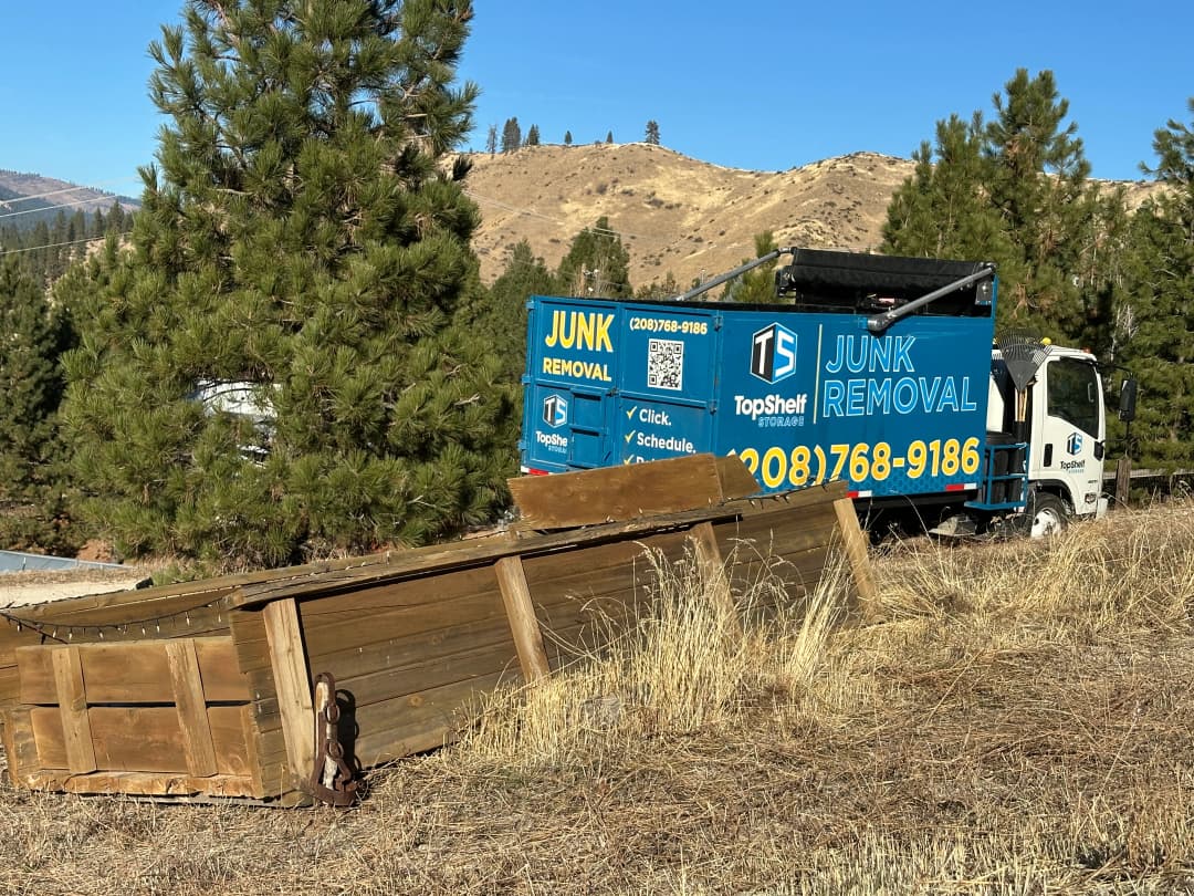 Top Shelf branded junk removal truck on a rural property with old wooden fence and farm debris ready for removal in Caldwell Idaho