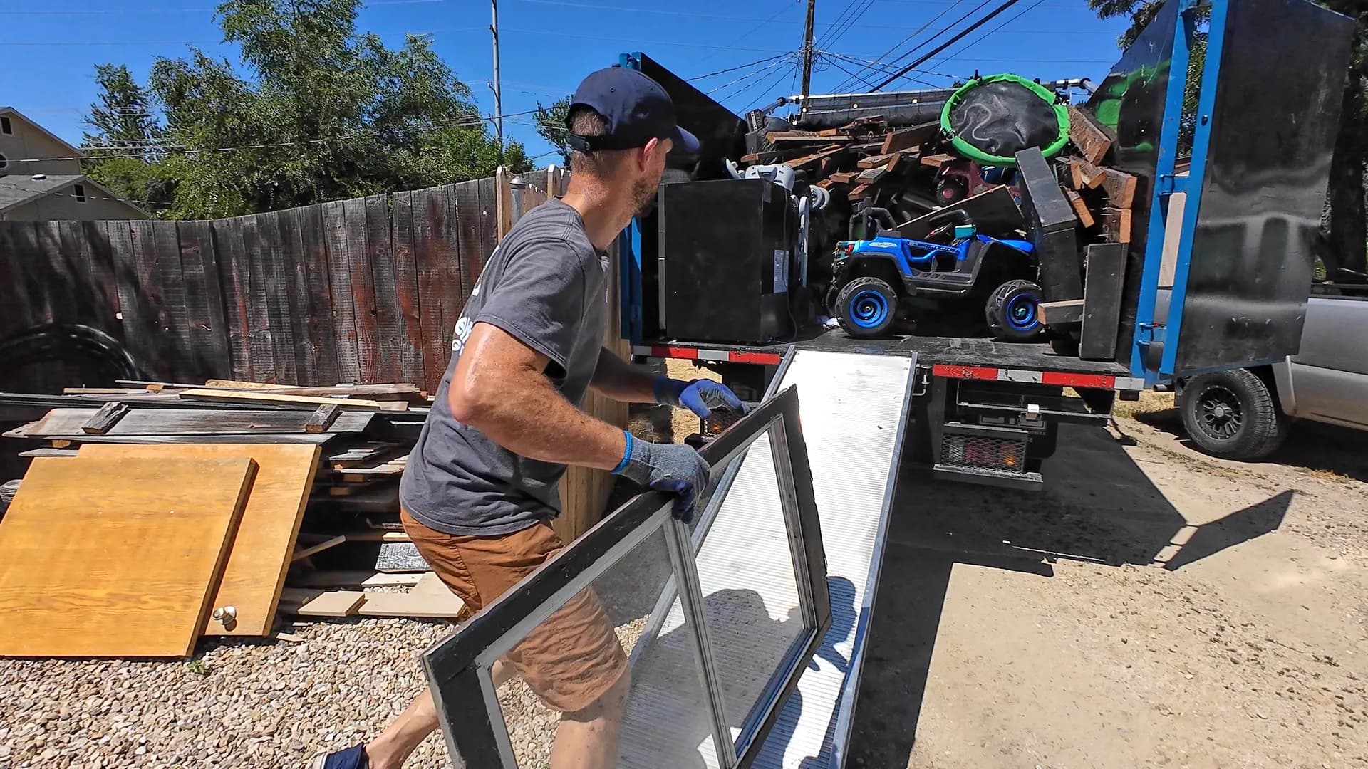 Top Shelf crew member loading wood panels and old window screens into the junk removal truck during a construction cleanup in Bridgetower, Meridian, Idaho