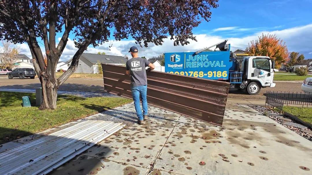 Top Shelf crew member in branded shirt carrying large metal siding panels to the junk removal truck during construction debris removal in Eagle Idaho