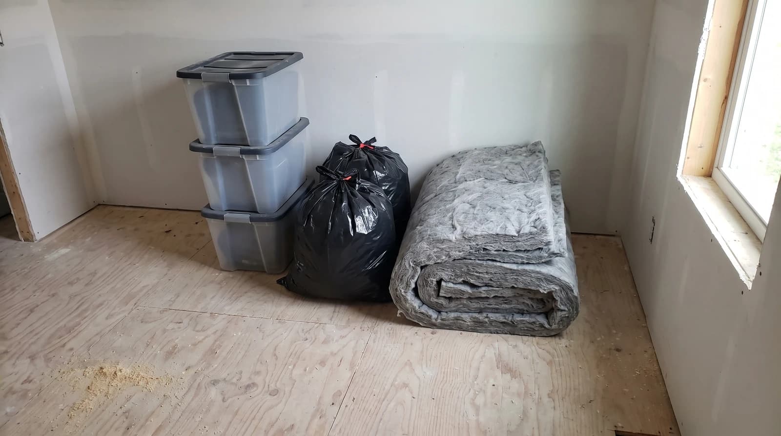 Sealed storage totes, tied contractor bags, and removed insulation stacked on a plywood floor after an attic cleanout in Nampa, Idaho