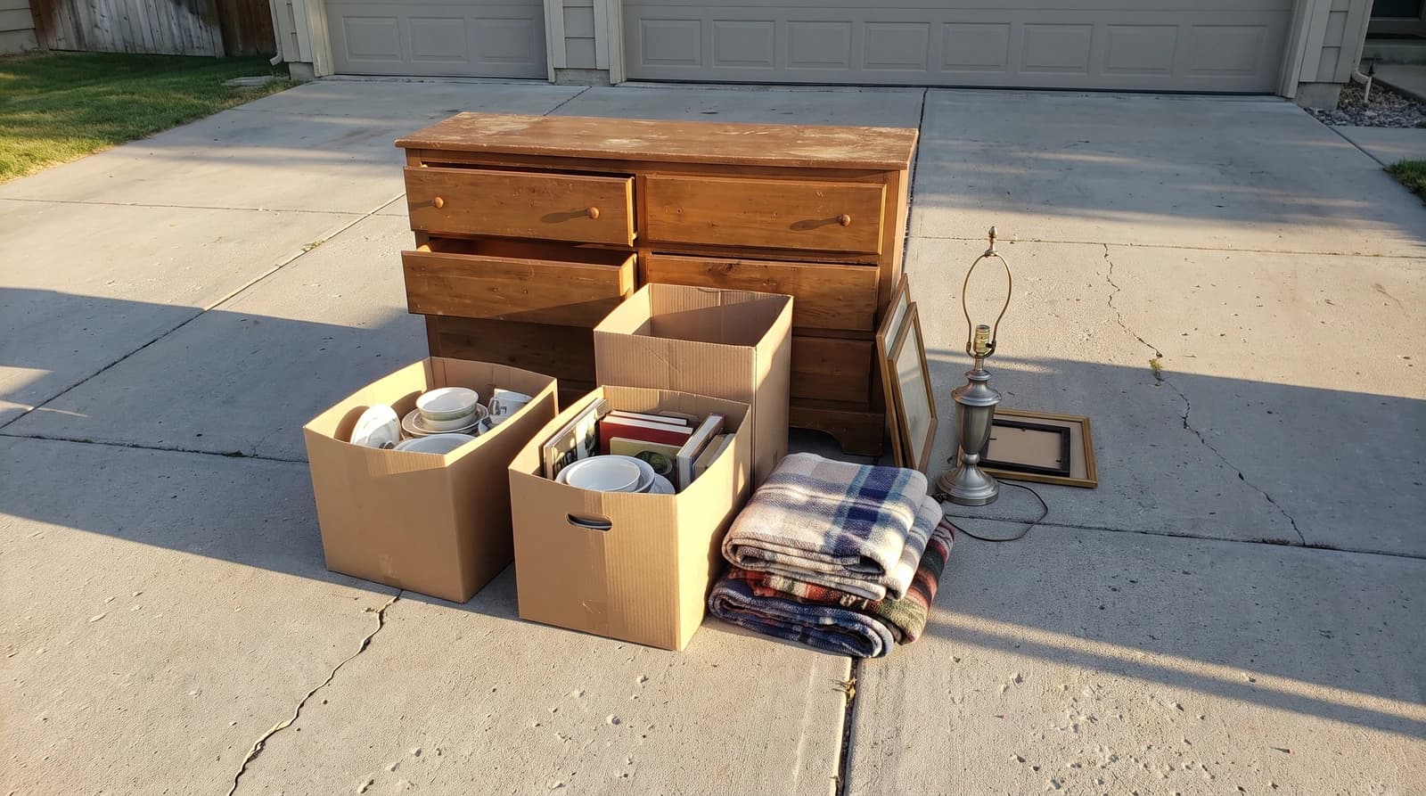 Leftover yard sale items, including a wooden dresser and boxes of dishes and books, stacked on a driveway in Nampa, Idaho, ready for bulk trash removal