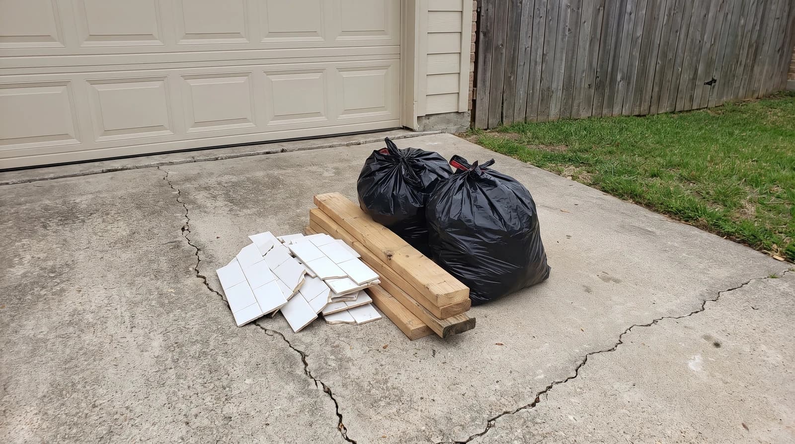 Leftover remodel debris including broken tile, cut lumber, and sealed contractor bags stacked on a driveway at a home in Boise, Idaho, waiting for construction cleanup