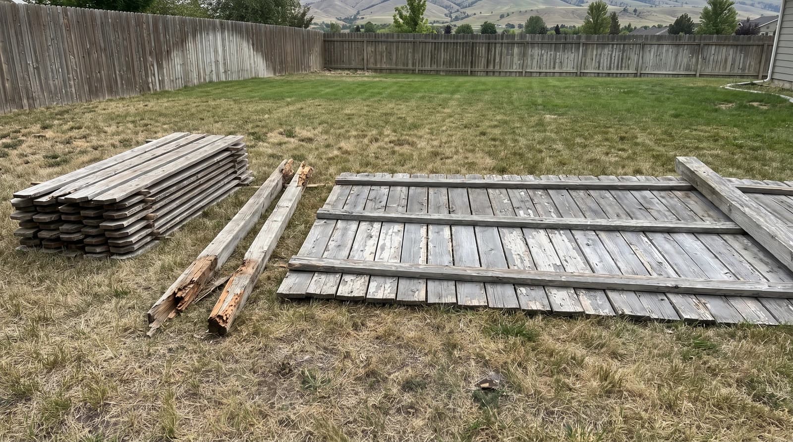 Storm-damaged wooden fence panels and stacked pickets lying on a backyard lawn in Boise, Idaho, ready for fence removal