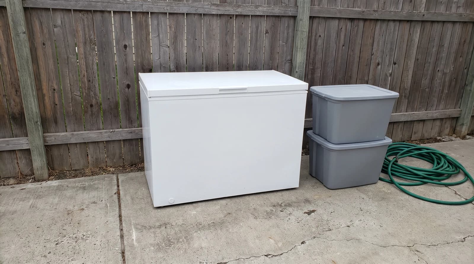 Old white chest freezer set out on a concrete driveway next to stacked storage totes at a home in Eagle, Idaho, ready for appliance removal.