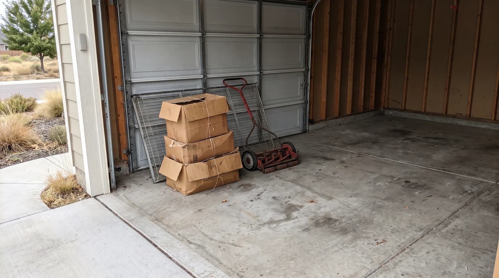 Cluttered two-car garage with old boxes, metal shelving, and a worn mower before a garage cleanout in Kuna, Idaho