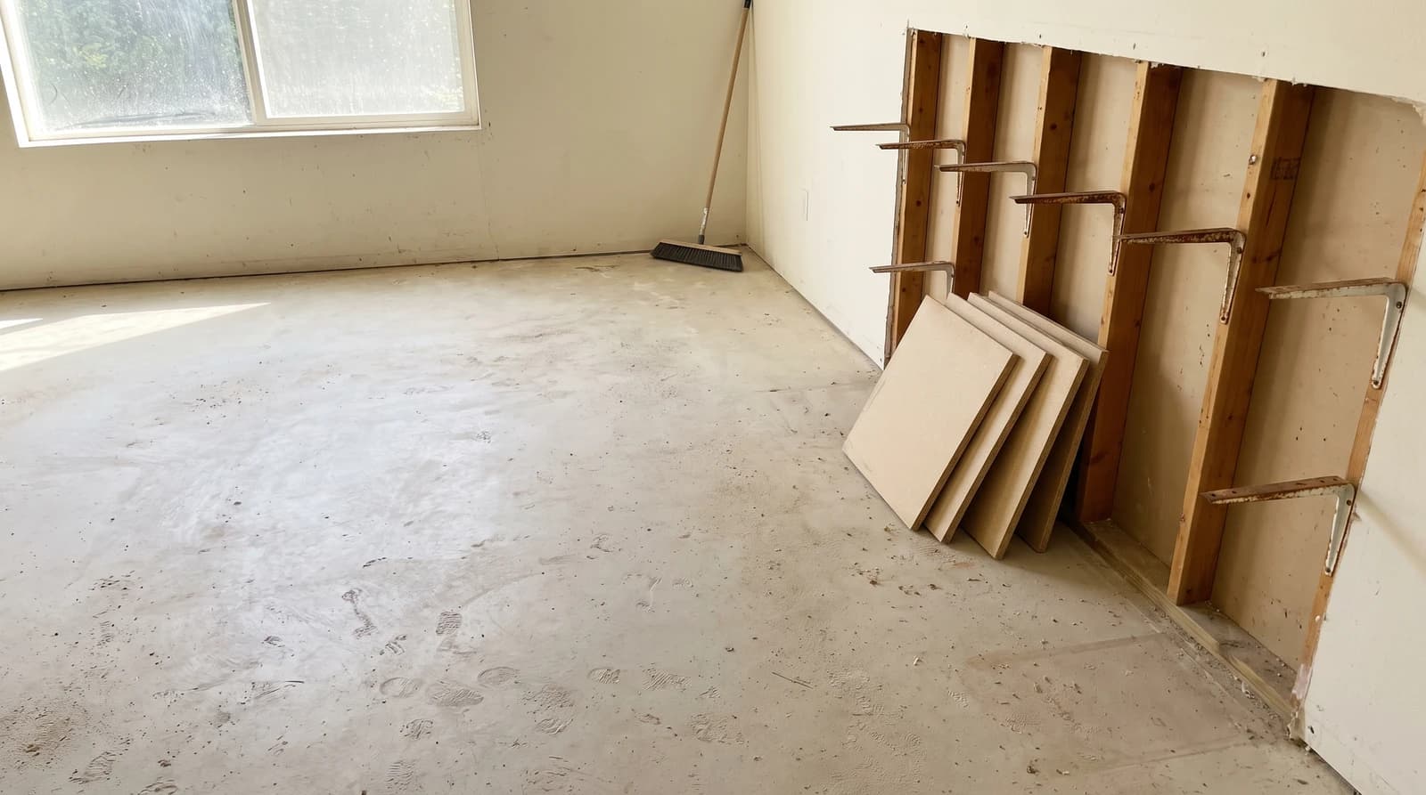 Emptied garage in Garden City, Idaho with bare concrete floor, leftover shelf brackets on the studs, and stacked particleboard shelf boards after a garage cleanout