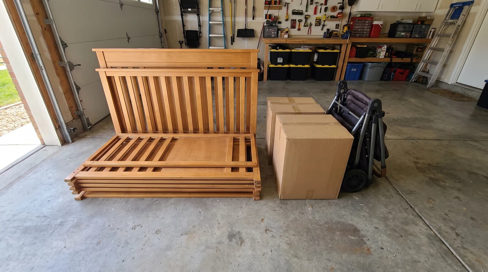 Disassembled crib panels stacked on a garage floor next to boxes and a folded stroller during a household junk removal cleanout in Meridian, Idaho