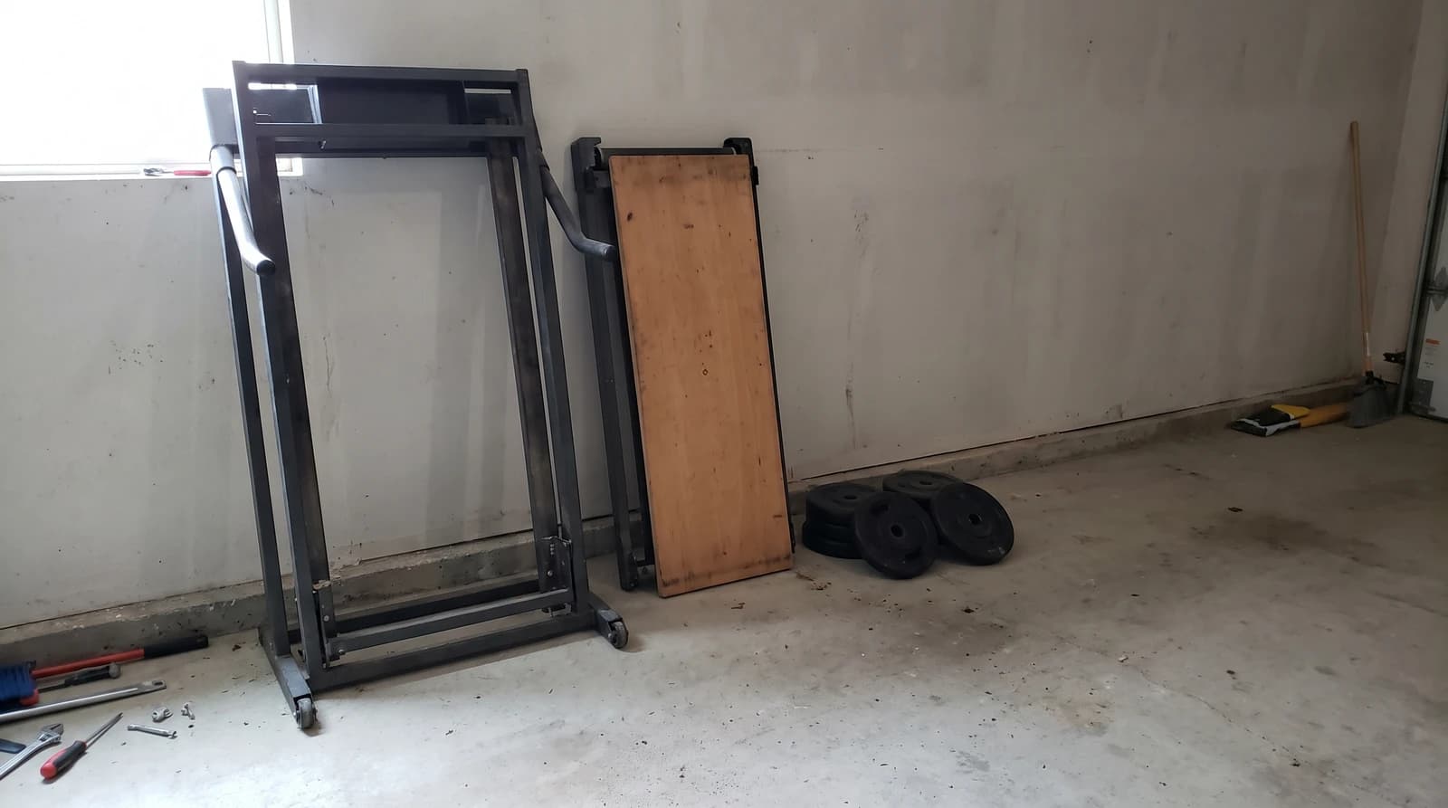 Disassembled treadmill frame leaning against a garage wall next to stacked weight plates during an exercise equipment removal job in Eagle, Idaho