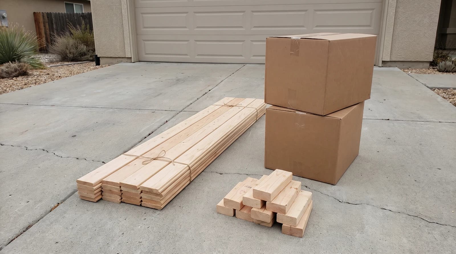 Leftover building materials sorted into neat stacks of tile boxes, trim boards, and scrap lumber on a driveway outside a home in Kuna, Idaho