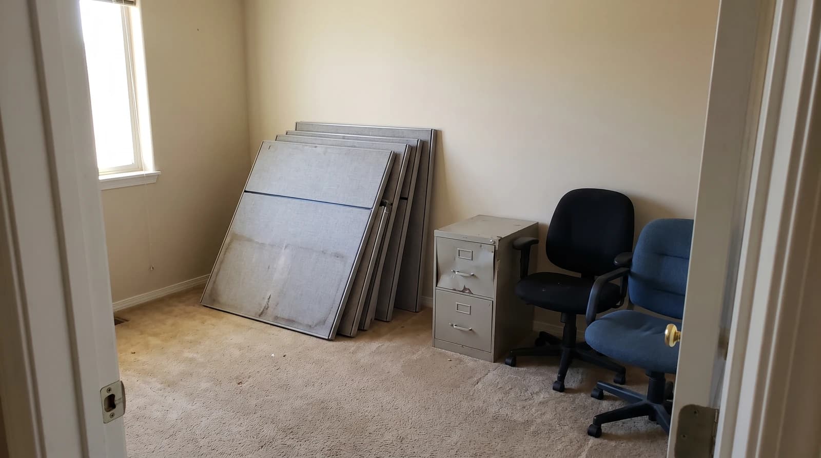 Stacked cubicle panels, a metal filing cabinet, and two office chairs waiting for furniture removal in an empty office in Eagle, Idaho