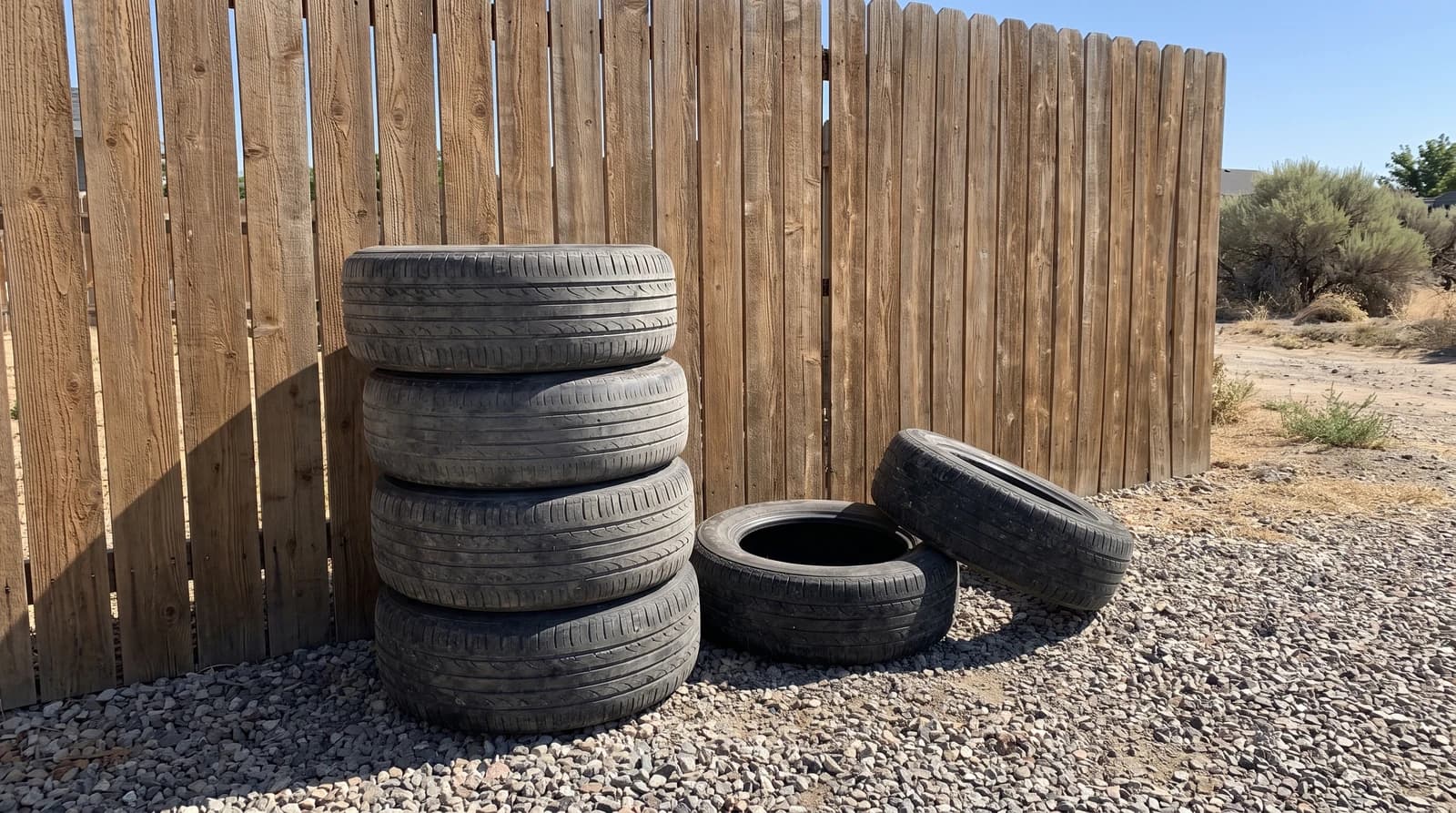 Stacked old passenger tires on a gravel driveway beside a wood fence at a home in Kuna, Idaho, ready for tire removal