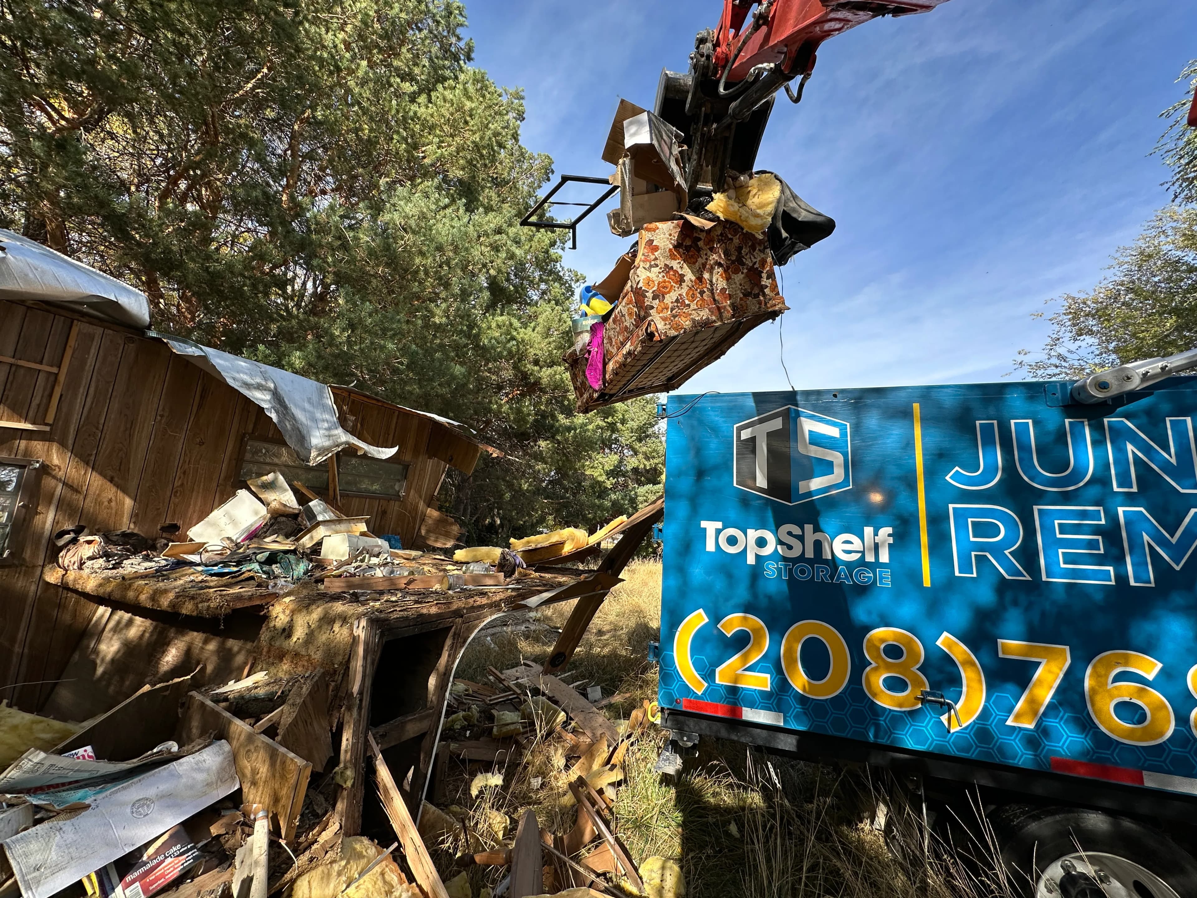 Top Shelf excavator grapple arm demolishing a structure and clearing debris with branded truck on site