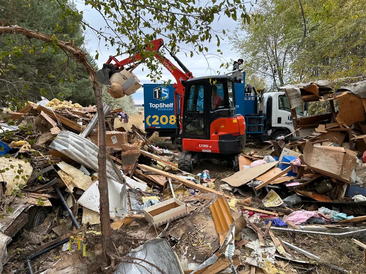Top Shelf Kubota excavator loading demolished structure debris into the branded truck surrounded by wood insulation and metal siding