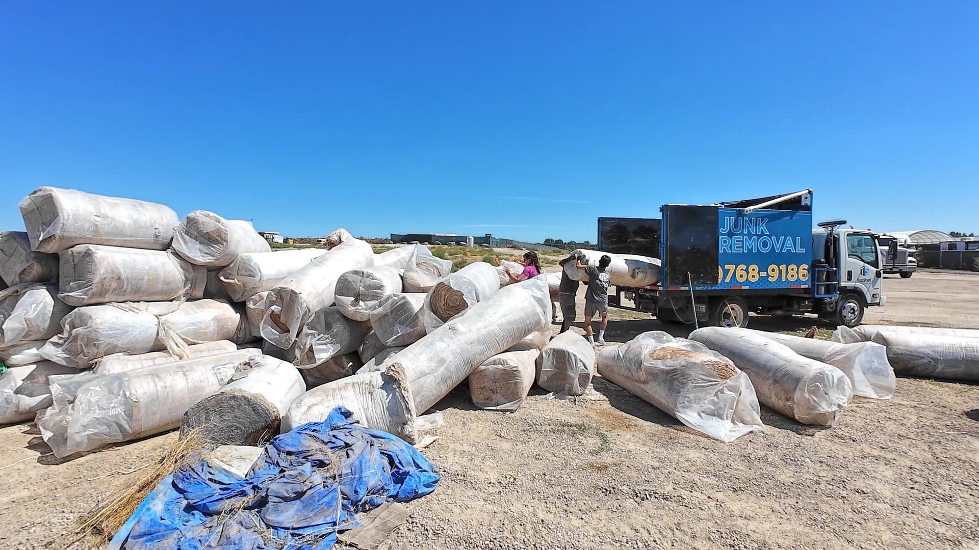 Top Shelf crew loading large rolls of commercial insulation into the branded junk removal truck at a job site in Nampa Idaho