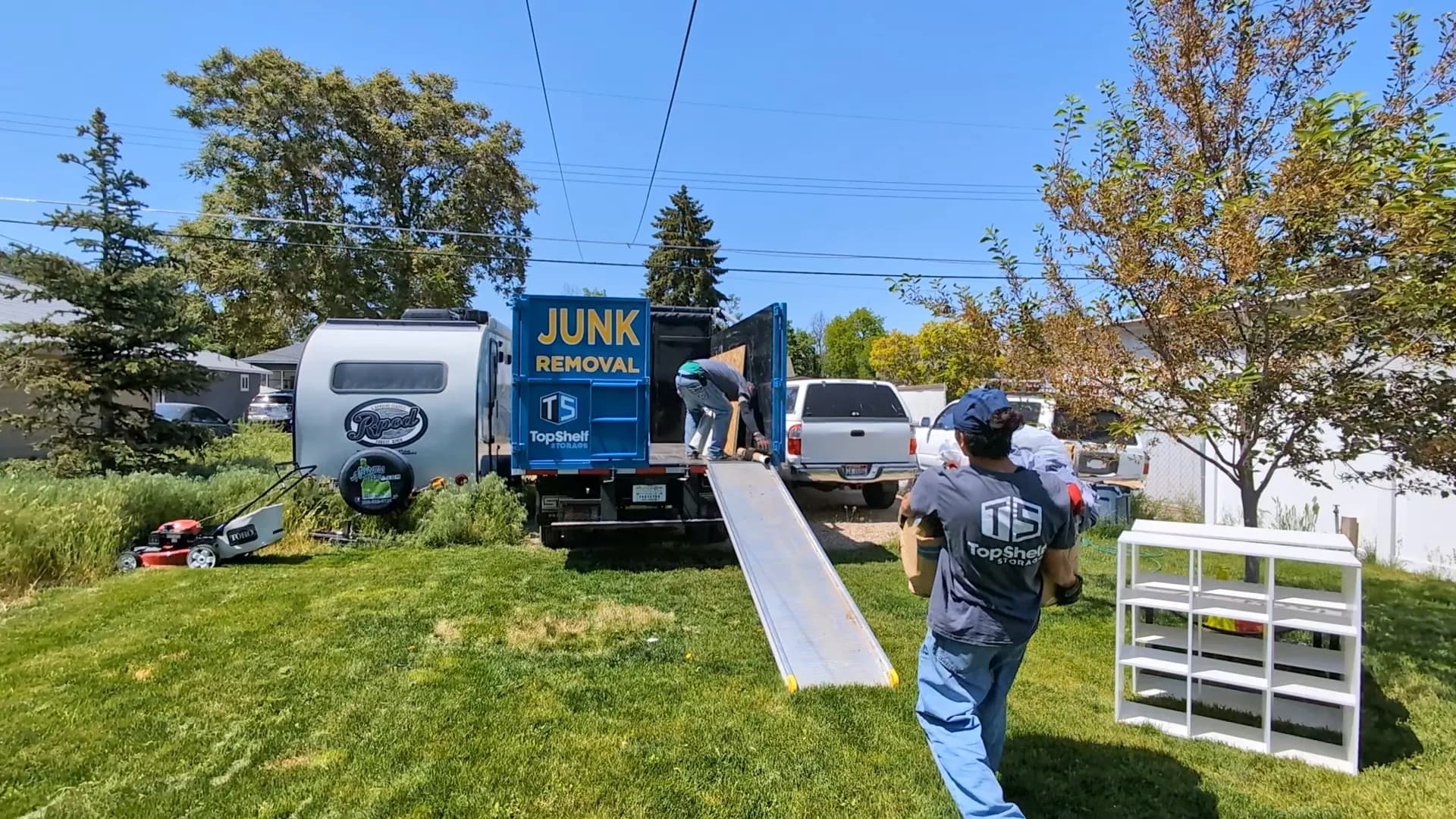 Top Shelf crew in branded shirts loading a white bookshelf into the junk removal truck at a residential property in Eagle Idaho