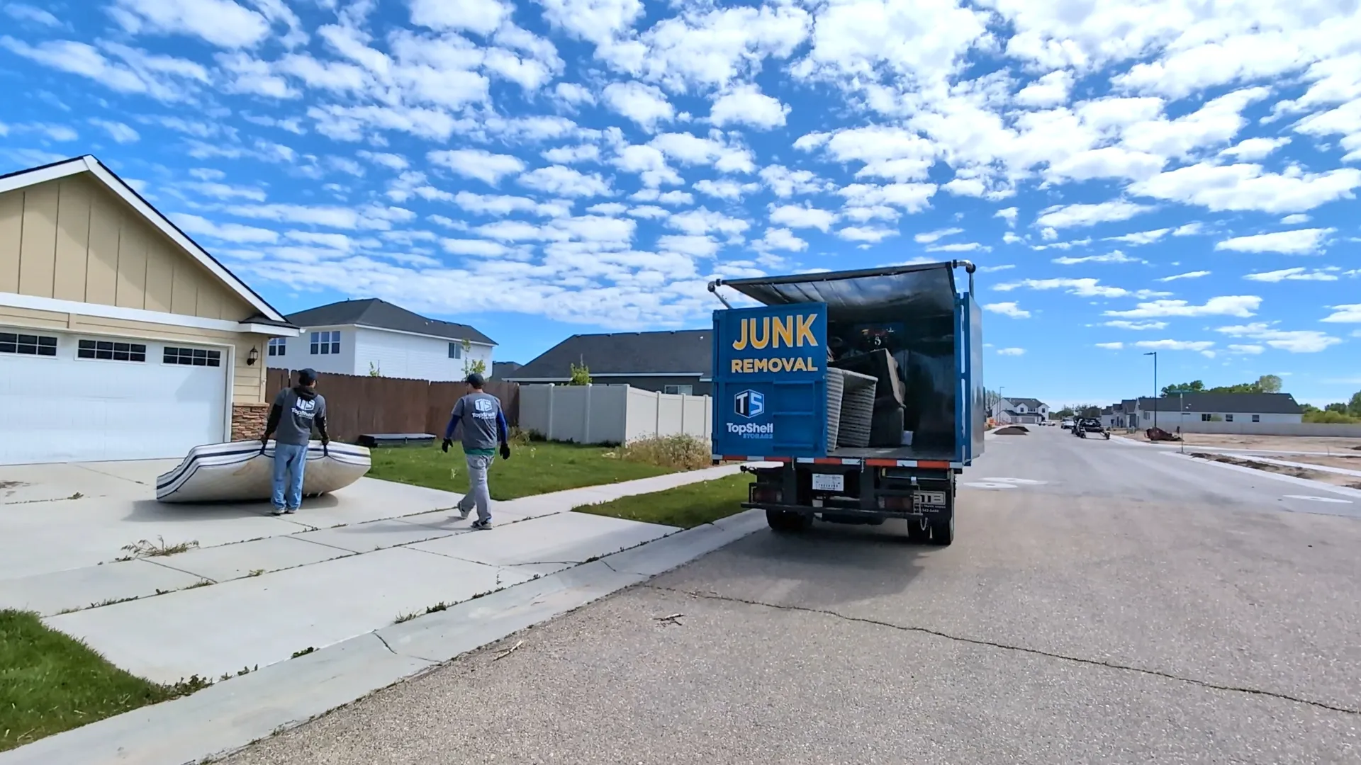 Two Top Shelf crew carrying a mattress to the branded junk removal truck in a new subdivision in Meridian Idaho
