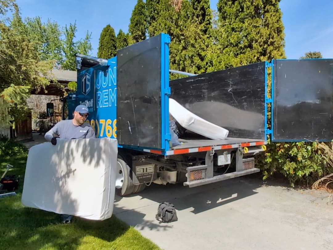 Top Shelf crew member loading a mattress into the branded junk removal truck at a residential driveway in Meridian Idaho