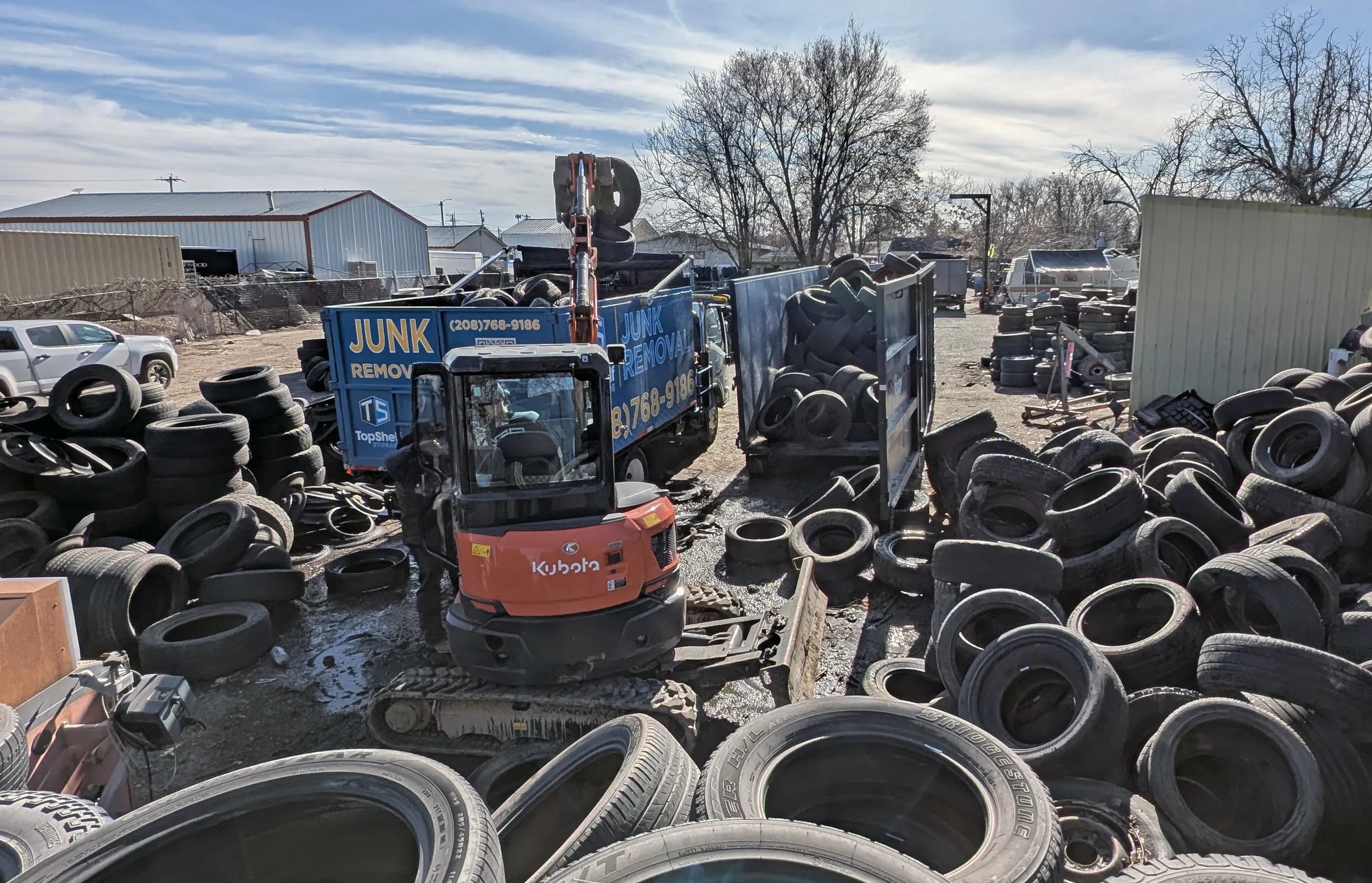 Top Shelf Kubota excavator and branded junk removal truck surrounded by hundreds of tires during a massive tire removal job in Garden City Idaho