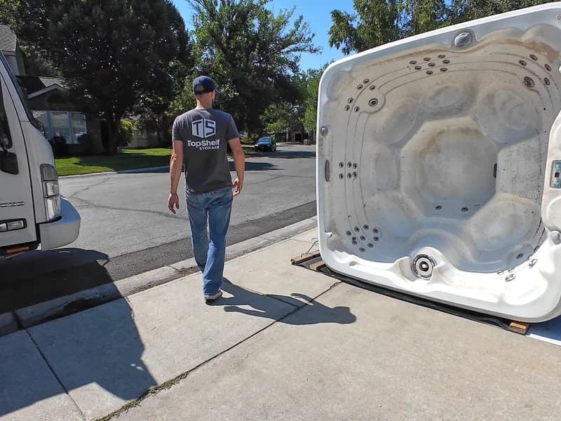 Top Shelf employee next to a tipped hot tub shell ready for loading beside the branded truck in Caldwell Idaho