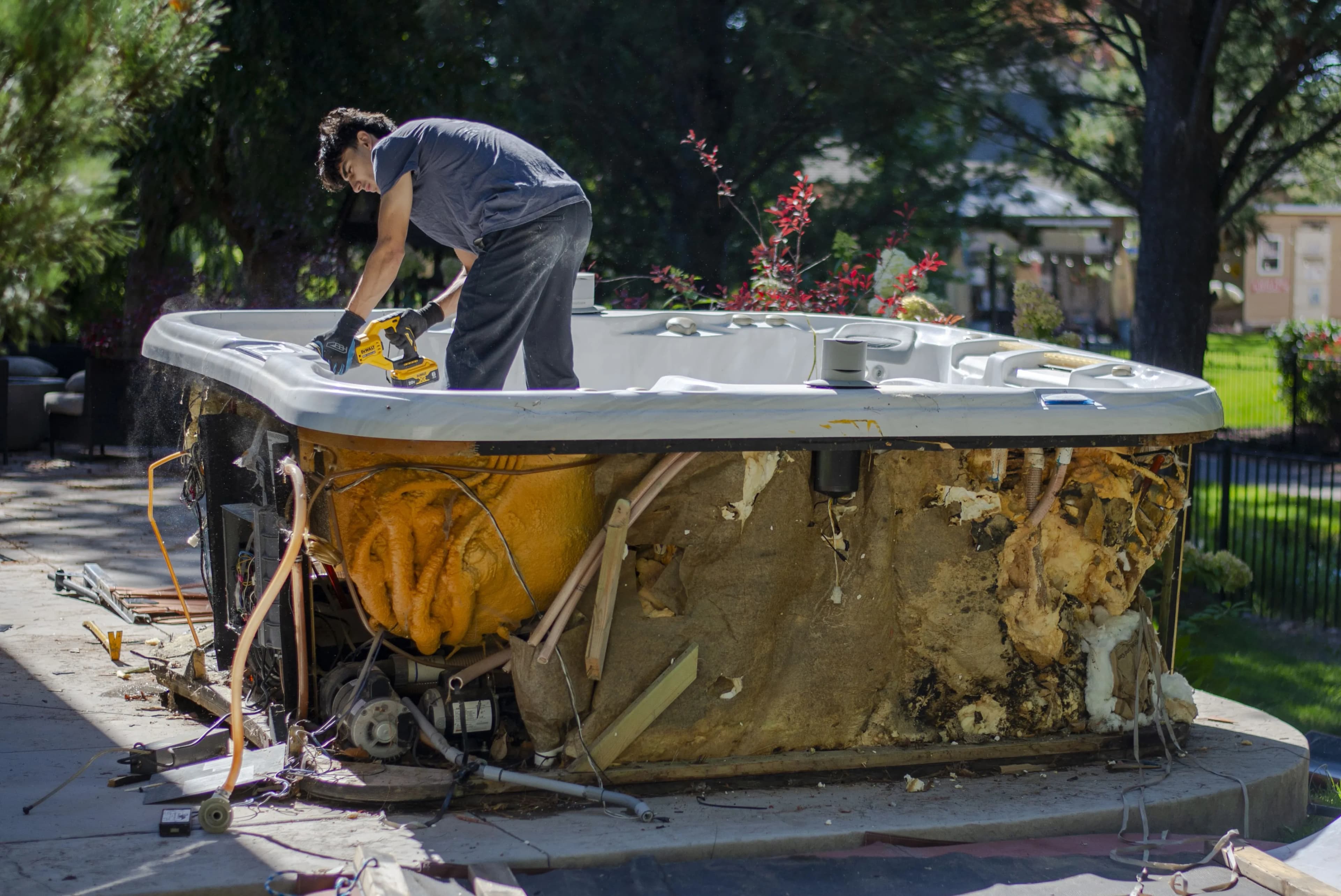 Top Shelf crew member using a reciprocating saw to demolish and cut apart a hot tub on a driveway in Caldwell Idaho