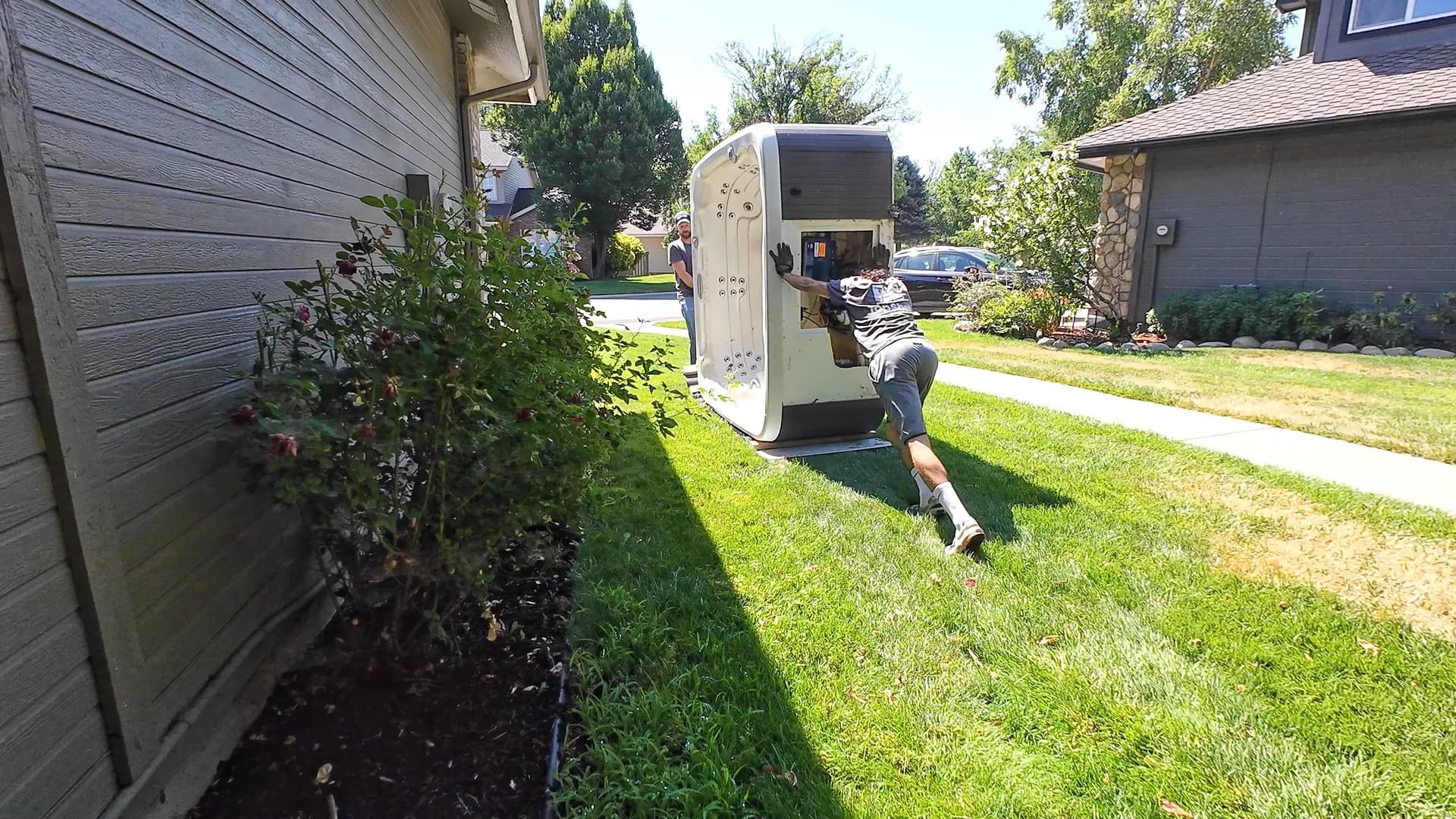 Top Shelf crew member pushing a hot tub on its side through a residential side yard during removal in Caldwell Idaho