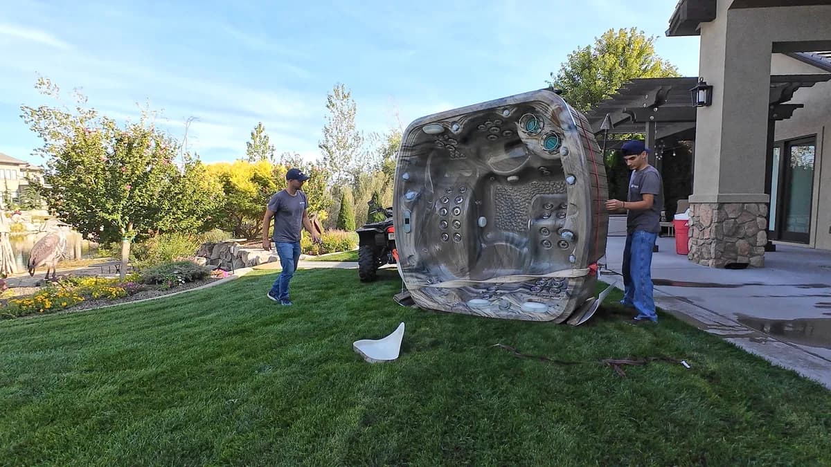 Two Top Shelf crew members tipping a large hot tub on its side for removal from a luxury landscaped backyard in Caldwell Idaho